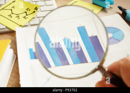 Vérification d'affaires. L'homme est à la recherche à travers une loupe sur les tableaux financiers. Banque D'Images