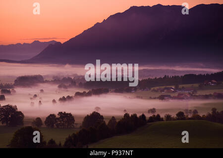 Matin de la campagne à couper le souffle du petit village bavarois couverts dans le brouillard. Vue panoramique des Alpes bavaroises au lever du soleil avec les montagnes majestueuses dans la zone Banque D'Images