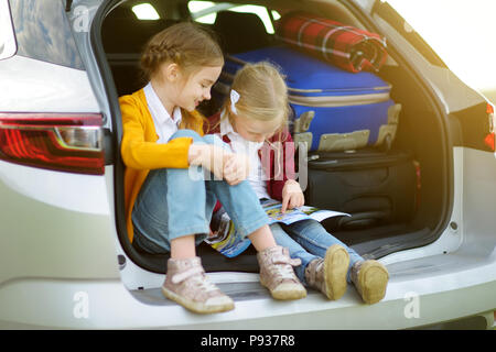 Deux adorables petites filles assise dans une voiture avant de partir en vacances avec leurs parents. Deux enfants à l'avant pour un voyage en voiture ou en voyage. Famille tr Banque D'Images