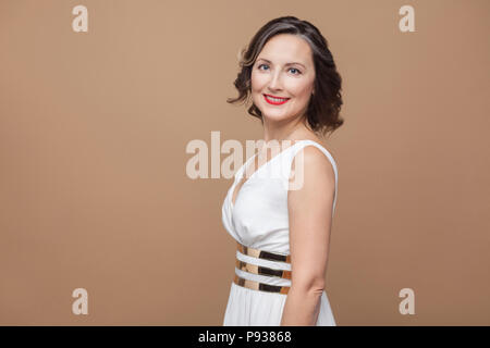 D'âge moyen assez rugueux smiley woman looking at camera. L'expression émotionnelle femme en robe blanche, les lèvres rouge foncé et curly hairstyle. Je, Studio shot Banque D'Images