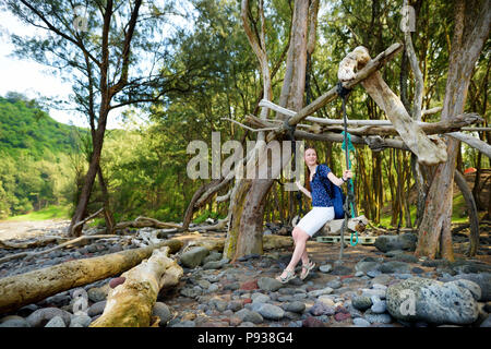 Young Woman relaxing on a swing artisanal sur plage rocheuse de la Vallée de Pololu sur la grande île d'Hawaii, USA Banque D'Images