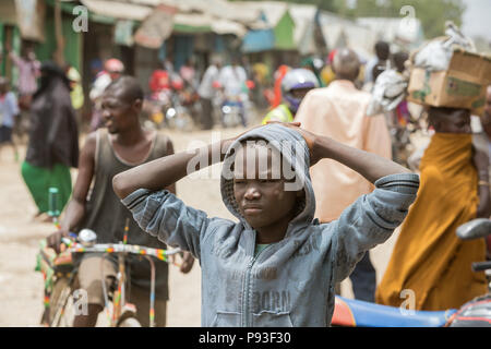 Kakuma, Kenya - Scène de rue avec des gens sur une longue route non revêtue. Portrait d'un garçon sérieux. Banque D'Images