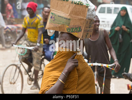 Kakuma, Kenya - Scène de rue avec des gens sur une longue route non revêtue. Portrait d'une femme portant une boîte en carton sur la tête. Banque D'Images