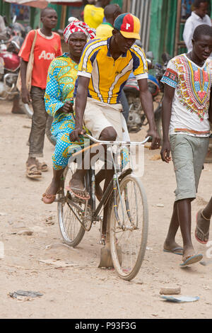 Kakuma, Kenya - Scène de rue. L'homme et de la femme faire de la bicyclette sur une route de terre. Banque D'Images