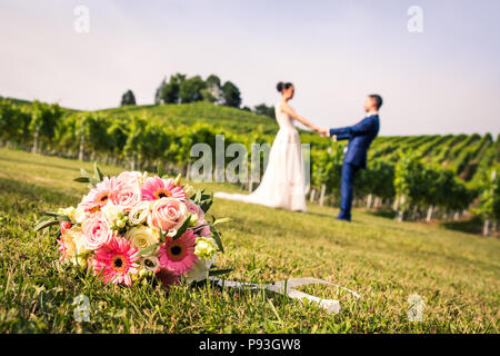 Bouquet de mariée rose et les jeunes mariés se tenant par la main dans l'arrière-plan flou sur une journée ensoleillée Banque D'Images