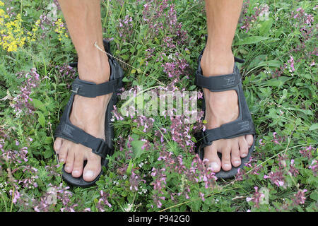 Photo de l'homme dans le sport sandales pieds sur l'herbe verte et des fleurs en arrière-plan. Banque D'Images