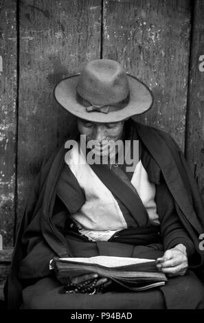 Un moine bouddhiste tibétain lit les écritures sur le BARKHOR () - Bazar tibétain de Lhassa, Tibet Banque D'Images