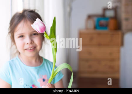 Fille avec une note de fleurs de printemps. Dans une maison confortable dans le salon par la fenêtre. Tulipes de couleurs différentes. Un cadeau d'une journée de la femme. Carte. Espace libre pour le texte ou une carte postale Banque D'Images