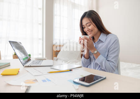 Asian businesswoman drinking coffee et tout en travaillant avec un ordinateur portable sur le tableau dans la chambre à la maison.Travail à domicile travail à domicile.concept concept Banque D'Images