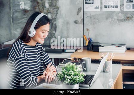 Young Asian businesswoman décontractée sur le bras de bureau reste posent avec ordinateur portable et l'écoute de la musique via la prise casque et penser à travailler ,travailler à domicile avec Banque D'Images