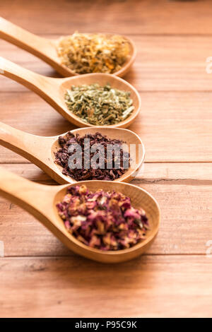 Cuillères en bois avec différentes herbes pour perfusion, style rustique, sur fond de bois. Banque D'Images