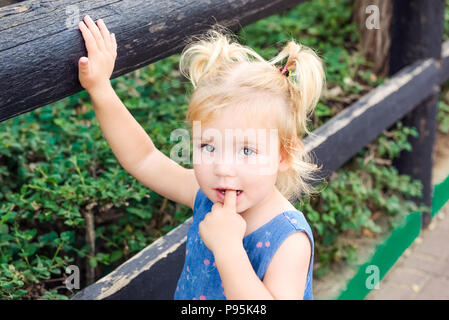 Close up Blondy toddler baby girl, looking at camera et mettant son doigt dans sa bouche - l'un des plus couramment observés dans les comportements, les habitudes childh Banque D'Images