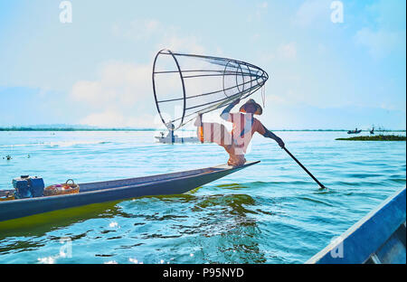 Lac Inle, MYANMAR - février 18, 2018 : pêcheur birman standard démontre de la pêche traditionnelle astuces avec une pagaie et moustiquaire conique, le févr. Banque D'Images