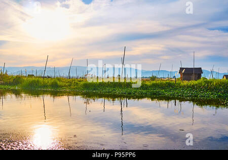 La surface claire d'Inle Lake reflète le ciel de coucher du soleil et de longs poteaux de ferme flottante, Ywama village, Myanmar. Banque D'Images