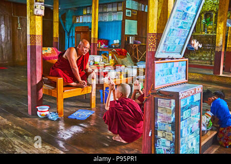 YWAMA, MYANMAR - février 18, 2018 : Le moine Bhikkhu assis sur une chaise dans le monastère de Nga Phe Chaung chats saut avec samaneras (moines novices), écrire un Banque D'Images