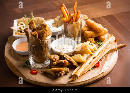 La bière Différentes collations : Anneaux de calamars, frites, Hot Wings, pain et sauces sur planche de bois Banque D'Images