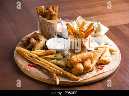 La bière Différentes collations : Anneaux de calamars, frites, Hot Wings, pain et sauces sur planche de bois Banque D'Images