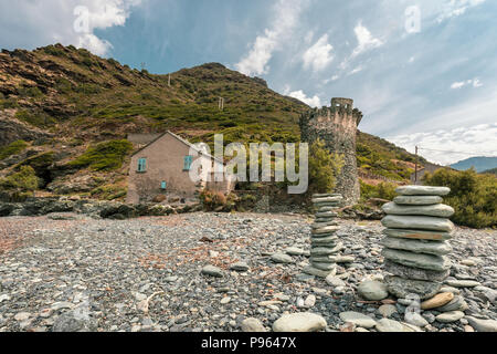 Deux cairns de pierre en face de la tour génoise de pierre ancienne et petite maison debout sur la côte à l'embouchure de la rivière d'Olmeta dans le village Banque D'Images