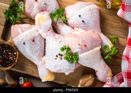 Les pilons de poulet sur une planche à découper avec épices et herbes. Les aliments crus prêts à la cuisson. Vue d'en haut. Banque D'Images