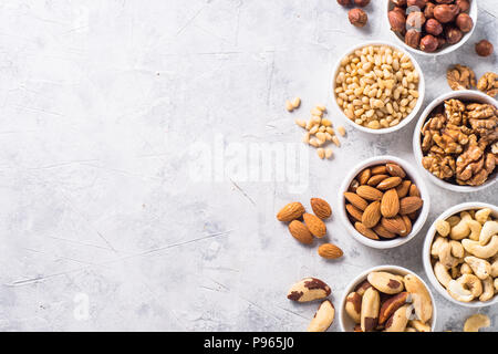 Assortiment de noix dans des bols. Cajou, noisettes, noix, amandes, noix du Brésil et noix de pin. Vue de dessus avec l'exemplaire de l'espace. Table en pierre de lumière. Banque D'Images