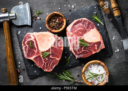 Steak de boeuf cru osso bucco sur fond ardoise noire. En viande. Vue d'en haut. Banque D'Images