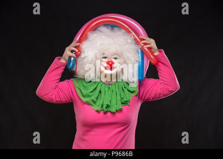 Funny clown aux cheveux hirsutes holding ballons colorés sur fond noir Banque D'Images