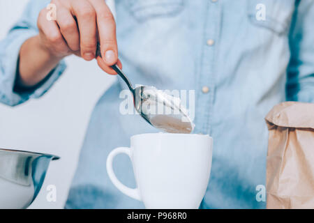 Portrait de femme cuillère de farine dans la cuvette blanche. Young woman wearing blue shirt mesurer la poudre avec cuillère à soupe. Banque D'Images