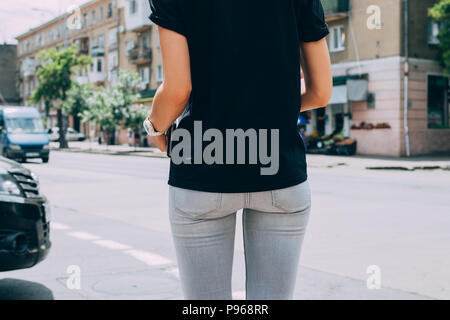 Mince Jeune femme debout devant la route urbaine avec des voitures, vue arrière. Close - up de femmes portant des jeans skinny gris et noir T-shirt dans la Banque D'Images