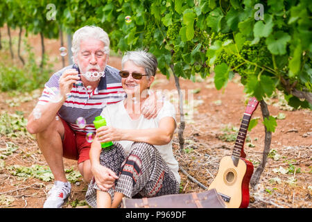 Belle caucasian couple senior homme et femme faire des bulles de savon ensemble pour jouer et s'amuser avec joie, heureux de l'emplacement en plein air dans la nature des activités de loisirs Banque D'Images