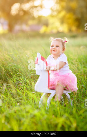 Belle petite fille en robe rose équitation sur cheval jouet en bois à l'extérieur Banque D'Images