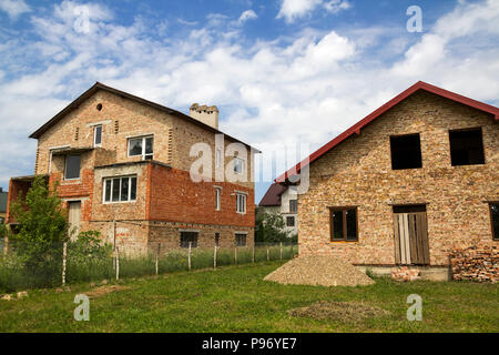 Terrain pour le développement dans les régions rurales de quartier. Deux nouveaux pas fini brique maisons chalets famille divisée avec temporaire grillage sur fond de ciel d'été. C Banque D'Images