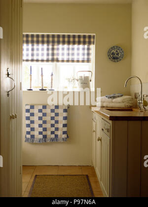 À carreaux blancs et bleus aveugles sur fenêtre au-dessus de sèche-serviettes avec une serviette bleu vérifiée dans une salle de bains cottage Banque D'Images