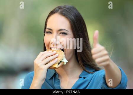 Happy woman mange un burger with Thumbs up looking at camera sur la rue Banque D'Images