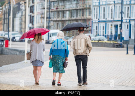 Pays de Galles Aberystwyth UK, lundi 16 juillet 2018 Royaume-Uni Météo : Après de nombreuses semaines de soleil presque constante et de temps exceptionnellement sec, les pluies sont revenues avec des gens à l'abri de l'averse vus sous leur parapluie comme ils marchent le long de la promenade à Aberystwyth, sur la côte ouest du pays de Galles Crédit photo : Keith Morris Alamy Live News Banque D'Images