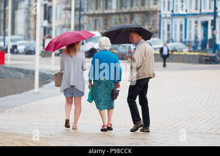 Pays de Galles Aberystwyth UK, lundi 16 juillet 2018 Royaume-Uni Météo : Après de nombreuses semaines de soleil presque constante et de temps exceptionnellement sec, les pluies sont revenues avec des gens à l'abri de l'averse vus sous leur parapluie comme ils marchent le long de la promenade à Aberystwyth, sur la côte ouest du pays de Galles Crédit photo : Keith Morris Alamy Live News Banque D'Images
