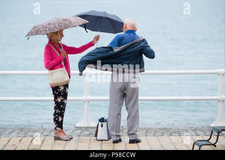 Pays de Galles Aberystwyth UK, lundi 16 juillet 2018 Royaume-Uni Météo : Après de nombreuses semaines de soleil presque constante et de temps exceptionnellement sec, les pluies sont revenues avec des gens à l'abri de l'averse vus sous leur parapluie comme ils marchent le long de la promenade à Aberystwyth, sur la côte ouest du pays de Galles Crédit photo : Keith Morris Alamy Live News Banque D'Images