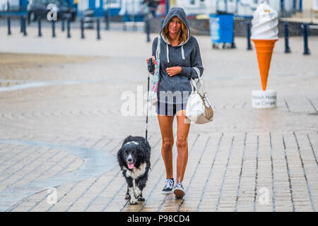 Pays de Galles Aberystwyth UK, lundi 16 juillet 2018 Royaume-Uni Météo : Après de nombreuses semaines de soleil presque constante et de temps exceptionnellement sec, les pluies ont repris avec une femme vu obtenir imbibé comme elle marche avec son chien le long de la promenade à Aberystwyth, sur la côte ouest du pays de Galles Crédit photo : Keith Morris Alamy Live News Banque D'Images