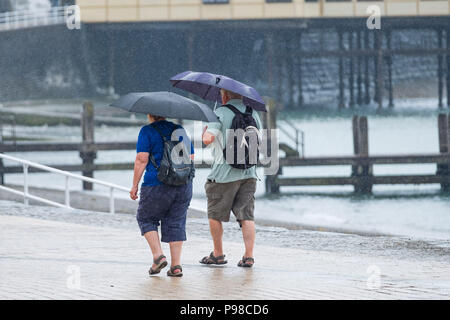 Pays de Galles Aberystwyth UK, lundi 16 juillet 2018 Royaume-Uni Météo : Après de nombreuses semaines de soleil presque constante et de temps exceptionnellement sec, les pluies sont revenues avec des gens à l'abri de l'averse vus sous leur parapluie comme ils marchent le long de la promenade à Aberystwyth, sur la côte ouest du pays de Galles Crédit photo : Keith Morris Alamy Live News Banque D'Images