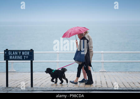 Pays de Galles Aberystwyth UK, lundi 16 juillet 2018 Royaume-Uni Météo : Après de nombreuses semaines de soleil presque constante et de temps exceptionnellement sec, les pluies sont revenues avec des gens à l'abri de l'averse vus sous leur parapluie comme ils marchent le long de la promenade à Aberystwyth, sur la côte ouest du pays de Galles Crédit photo : Keith Morris Alamy Live News Banque D'Images