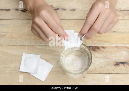 Main femme tomber comprimé effervescent dans un verre d'eau sur la table en bois Banque D'Images