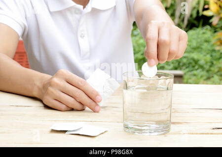 Femme passant comprimé effervescent dans le verre d'eau sur la table en bois Banque D'Images