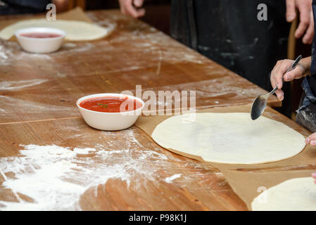 Close-up des mains des enfants préparer des pizzas. Les enfants sur la base de légumes et de fromage à pizza Banque D'Images