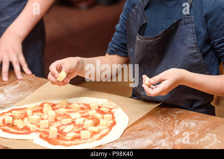 Close-up des mains des enfants préparer des pizzas. Les enfants sur la base de légumes et de fromage à pizza Banque D'Images