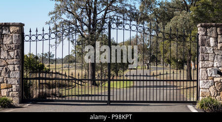 Metal entrée portes d'entrée de la propriété rurale mis en grès brique clôture avec l'eucalyptus gum arbres en arrière-plan Banque D'Images