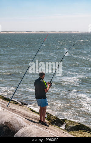 L'homme est debout sur une pierre angulaire de la mer avec une canne à pêche à la main Banque D'Images