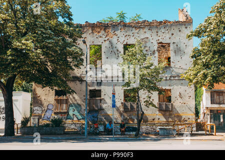 Deux sections locales s'asseoir devant les restes d'une coquille d'artillerie, la façade de l'immeuble, à Mostar, Bosnie-Herzégovine Banque D'Images