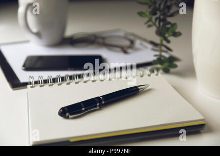 Table de bureau moderne blanc avec le smartphone et tasse de café. Blank page du bloc-notes à l'avant. travailler, l'écriture concept Banque D'Images