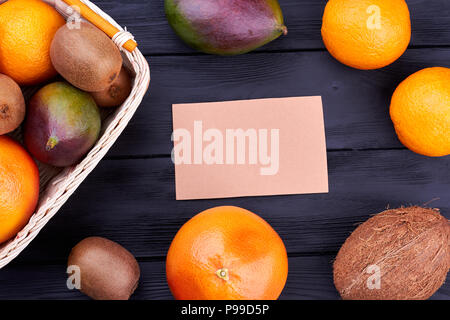 Assortiment de fruits tropicaux et de carte vierge. Variété de fruits colorés et feuille de papier vide sur fond de bois sombre, vue du dessus. Banque D'Images