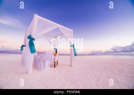 Dîner romantique table set-up pour un couple en lune de miel sur la plage sous le ciel au coucher du soleil. Mariage et lune de miel exotique concept Banque D'Images