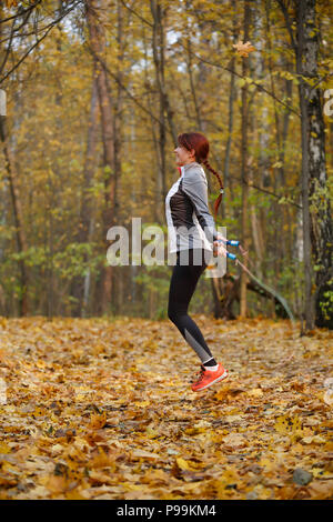 Grande photo de jeune brunette sautant avec corde à forêt d'automne Banque D'Images